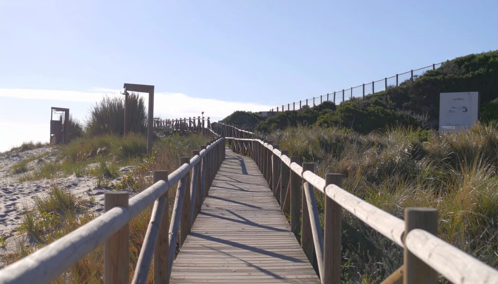 Spanien – Strandurlaub: Holzbohlenweg mit Strandduschen und Dünengras