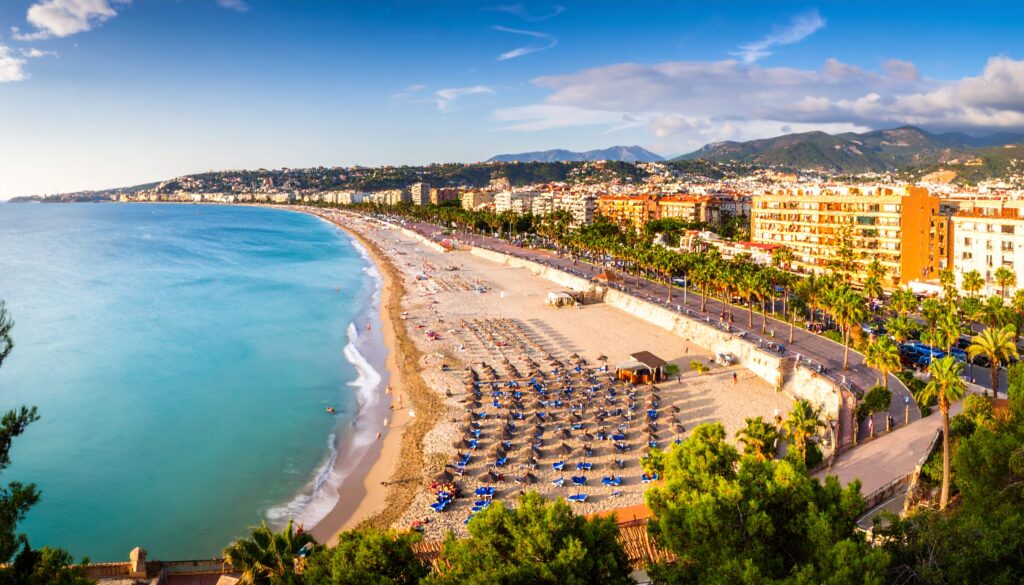 Spanien – Pauschalreisen: panorama einer küstenpromenade mit geordneten sonnenschirmen und resort-skyline
