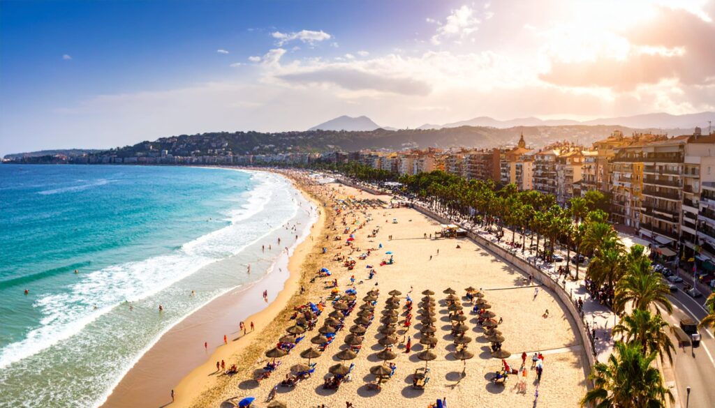 Spanien – Strandurlaub: Panorama einer abendlichen Küstenpromenade mit geordneten Sonnenschirmen und sanften Wellen